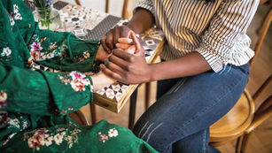 Two women’s hands clasp as they sit at a table and have a serious conversation about respecting boundaries.