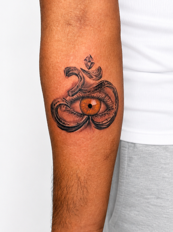 Detailed Om symbol tattoo with a realistic eye at its center on the forearm