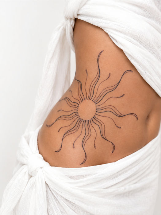 Fine line sun tattoo with long wavy rays covering the side ribs