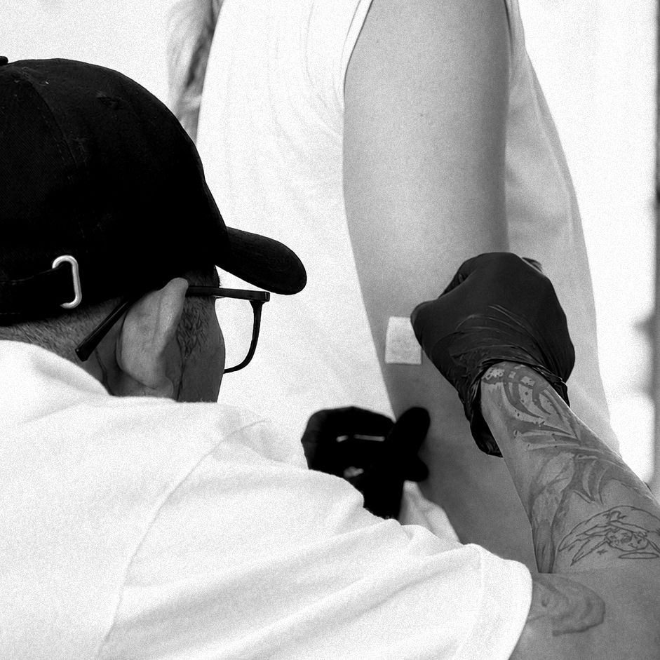 Tattoo artist inking a fine line Balinese mask design on a client's forearm