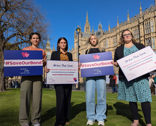 Four mums stand on the lawn in front of UK Parliament holding campaign boards for the Save Our Bond campaign
