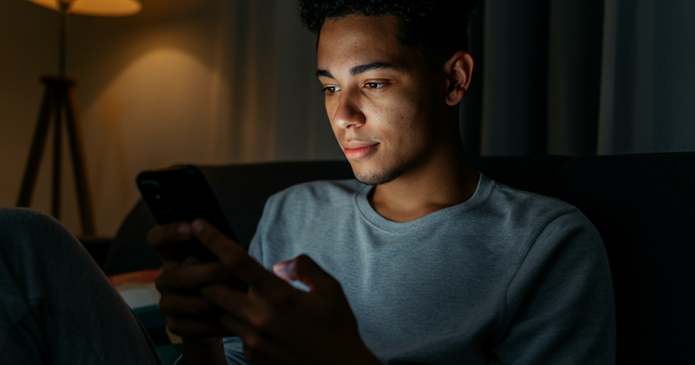 Jovem da geração Z usando o celular no sofá em um quarto escuro, com o rosto iluminado pela tela, representando a busca por imóveis online à noite.