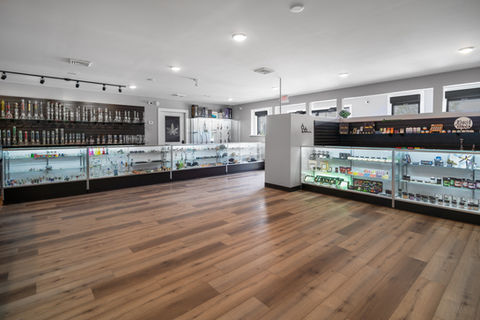 Wide-angle store photo with glass displays containing bongs, cannabis flower, containers, and more