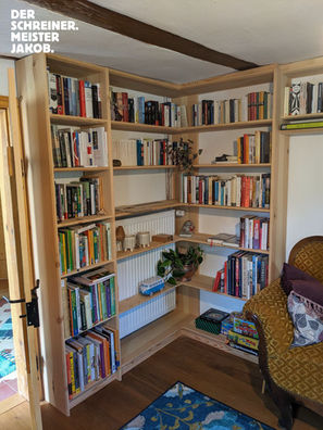 Zu sehen ist ein offenes Bücherregal in einem hellen Holz