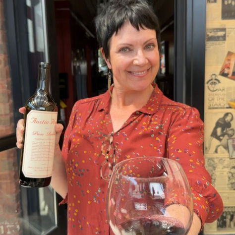 Kelly Fisk holding a bottle of Austin Hope cabernet with an oustretched hand holding a glass full of the cabernet.