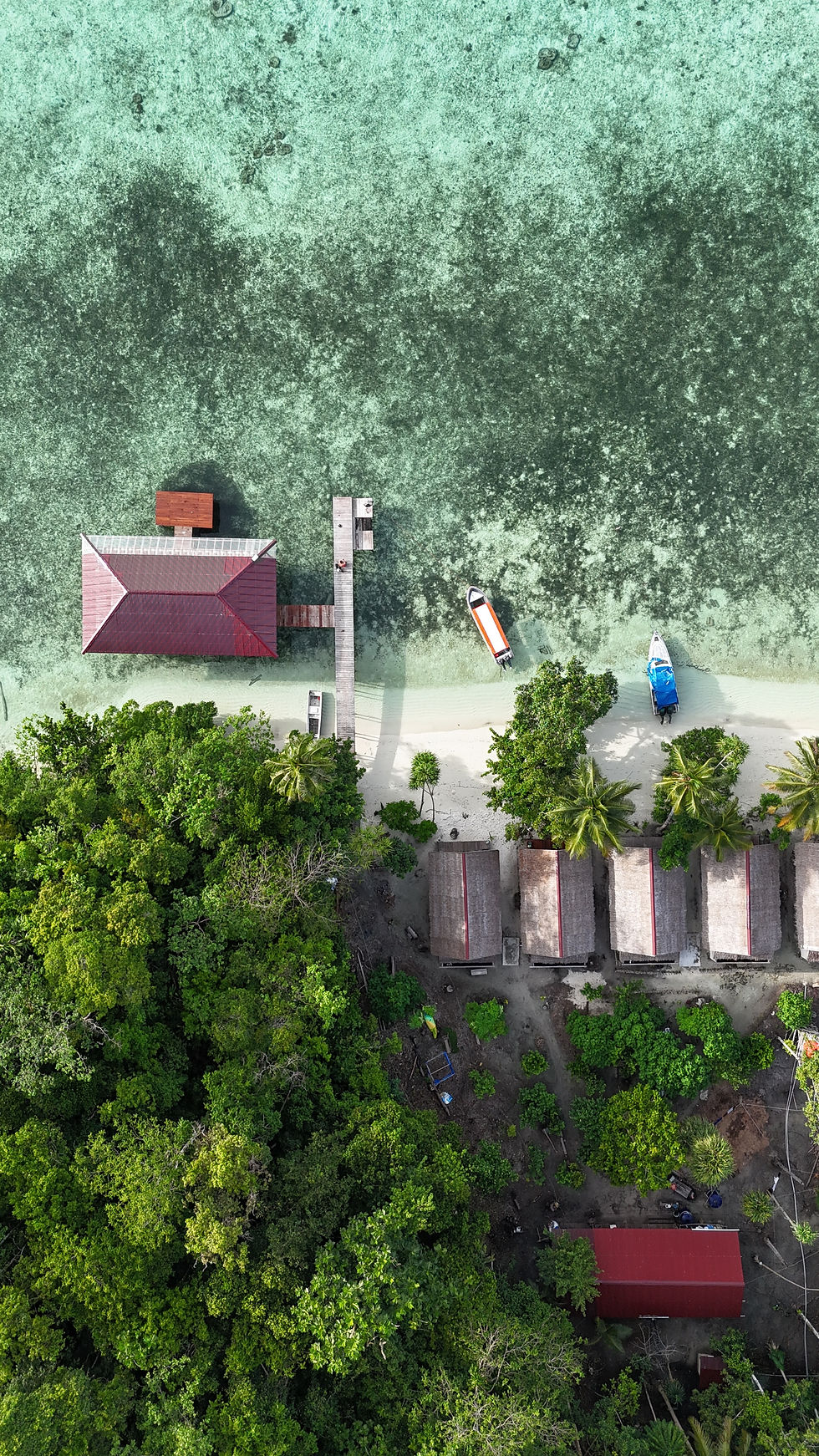 Luxury overwater resort in Raja Ampat surrounded by crystal-clear turquoise lagoon and lush tropical islands at sunset.