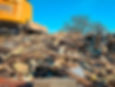 Yellow excavator demolishing a building, wood debris and clear blue sky, scrap uae.