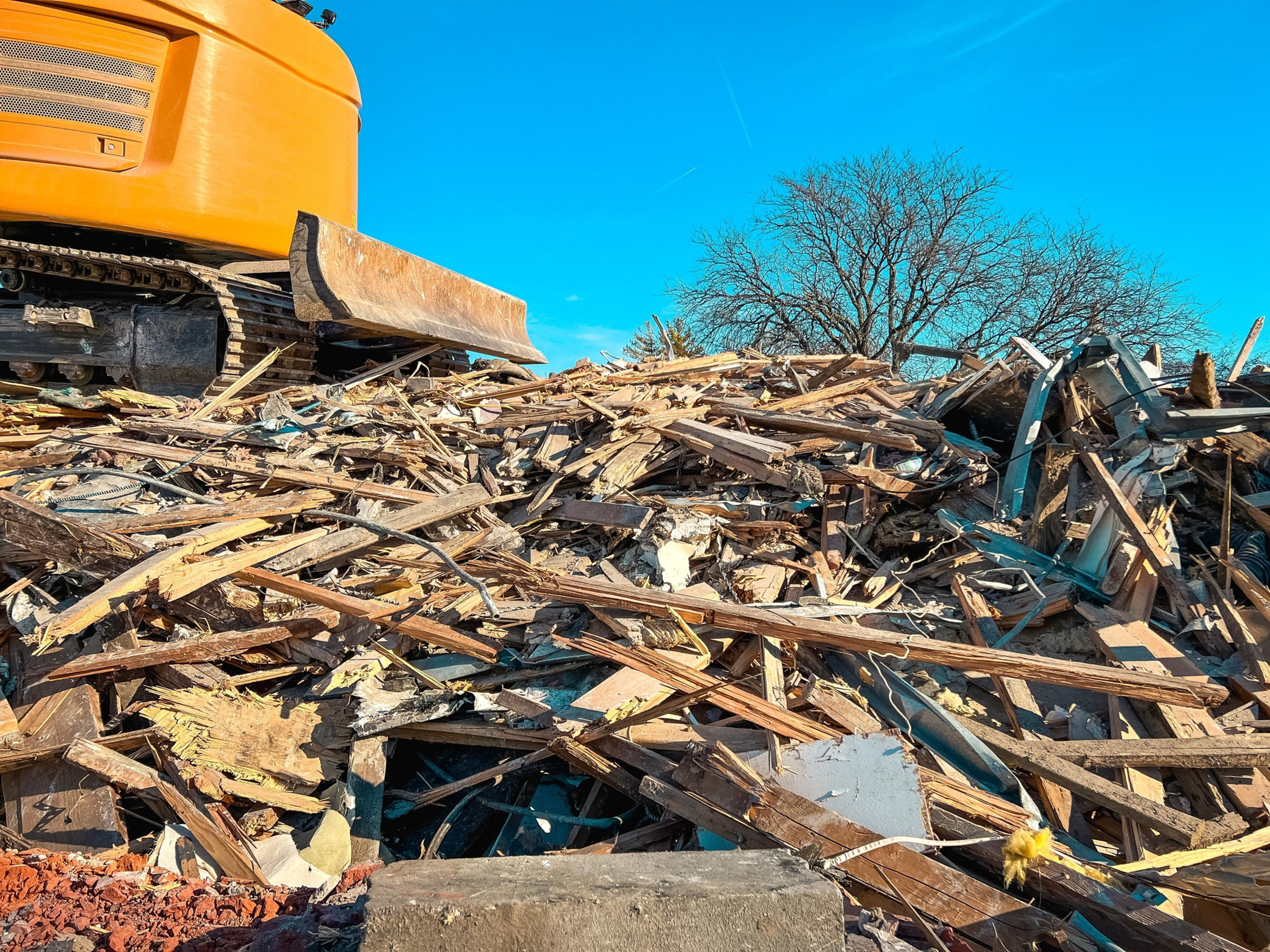 Excavator amidst Construction & Demolition Waste clearing debris under a bright sky.