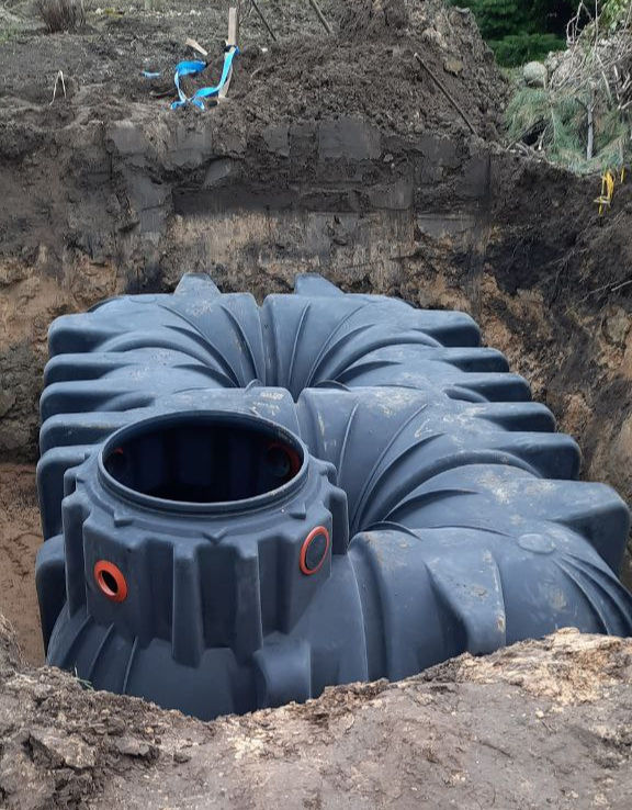 Zisterne aus schwarzen Plastik beim Einbau. Sie steht in einer Erdgrube.