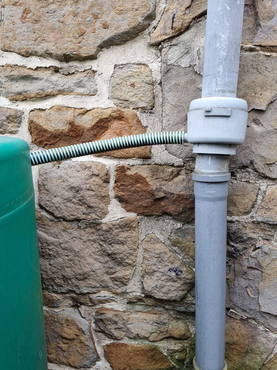 Fallrohr mit einem Regensammler. Ein grüner Schlauch geht davon ab in eine grüne Regentonne aus Plastik