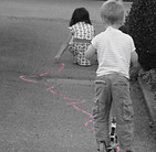 Zero Waste mit Kindern: zwei Kindern spielen auf der Straße: eines malt Kreide, das andere fährt mit dem Roller