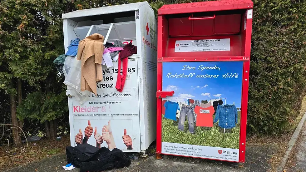 Zwei Altkleidercontainer an einem öffentlichen Standort in Bayern. Bayerisches rotes Kreuz und Malteser sammeln hier. Der Container vom roten Kreuz quilt über und die Klamotten hängen mittlerweile nass aus dem Container und liegen auf dem nassen Boden, umgeben von Abfall
