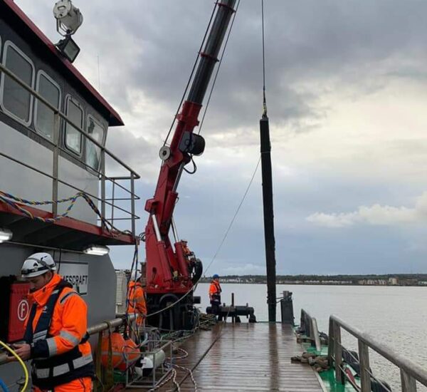 Crane on barge lowering a caisson into water with workers