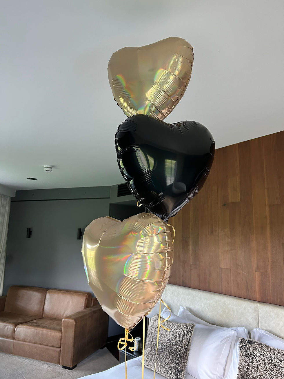 Three heart-shaped balloons, gold and black, a Valentine's Day party decoration indoors.