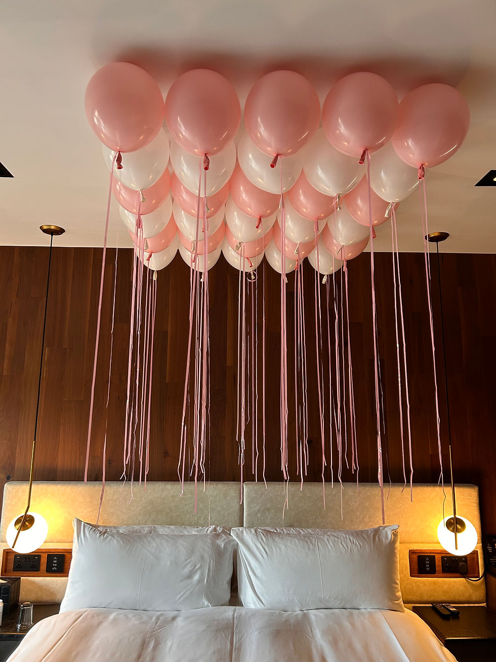 Pink and white balloons hanging above a bed, Valentine's Day decor.