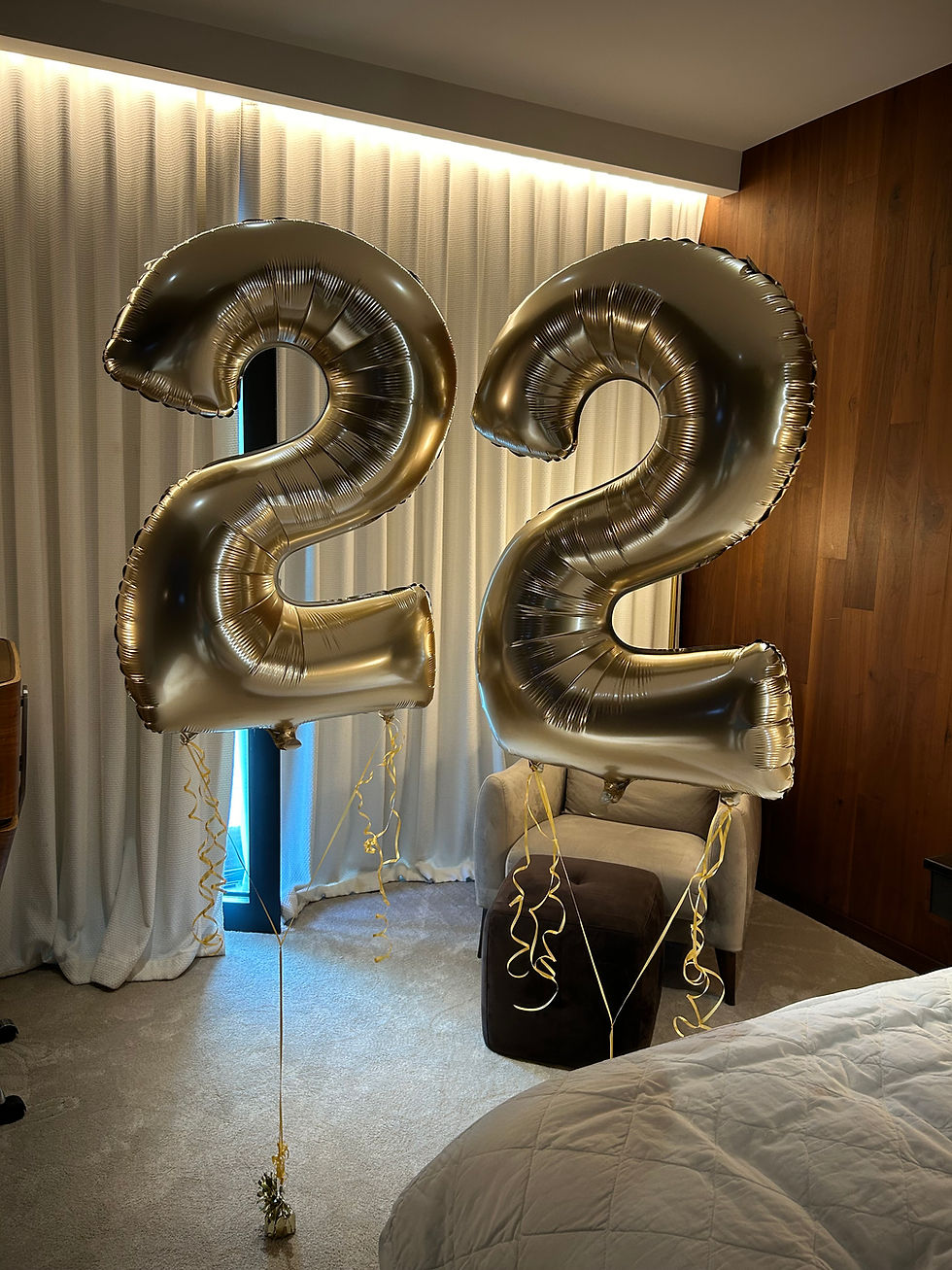 Golden 22 balloons displayed indoors with a bed and a chair in the background.