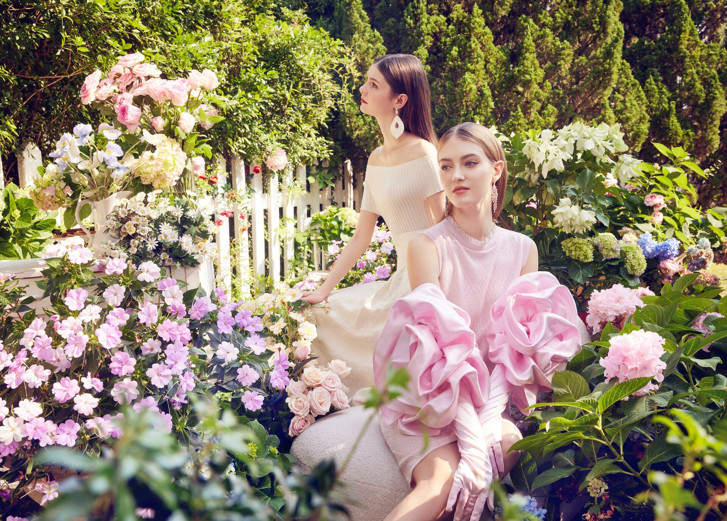 Models in Cashmere Song dresses, surrounded by vibrant flowers in a lush garden