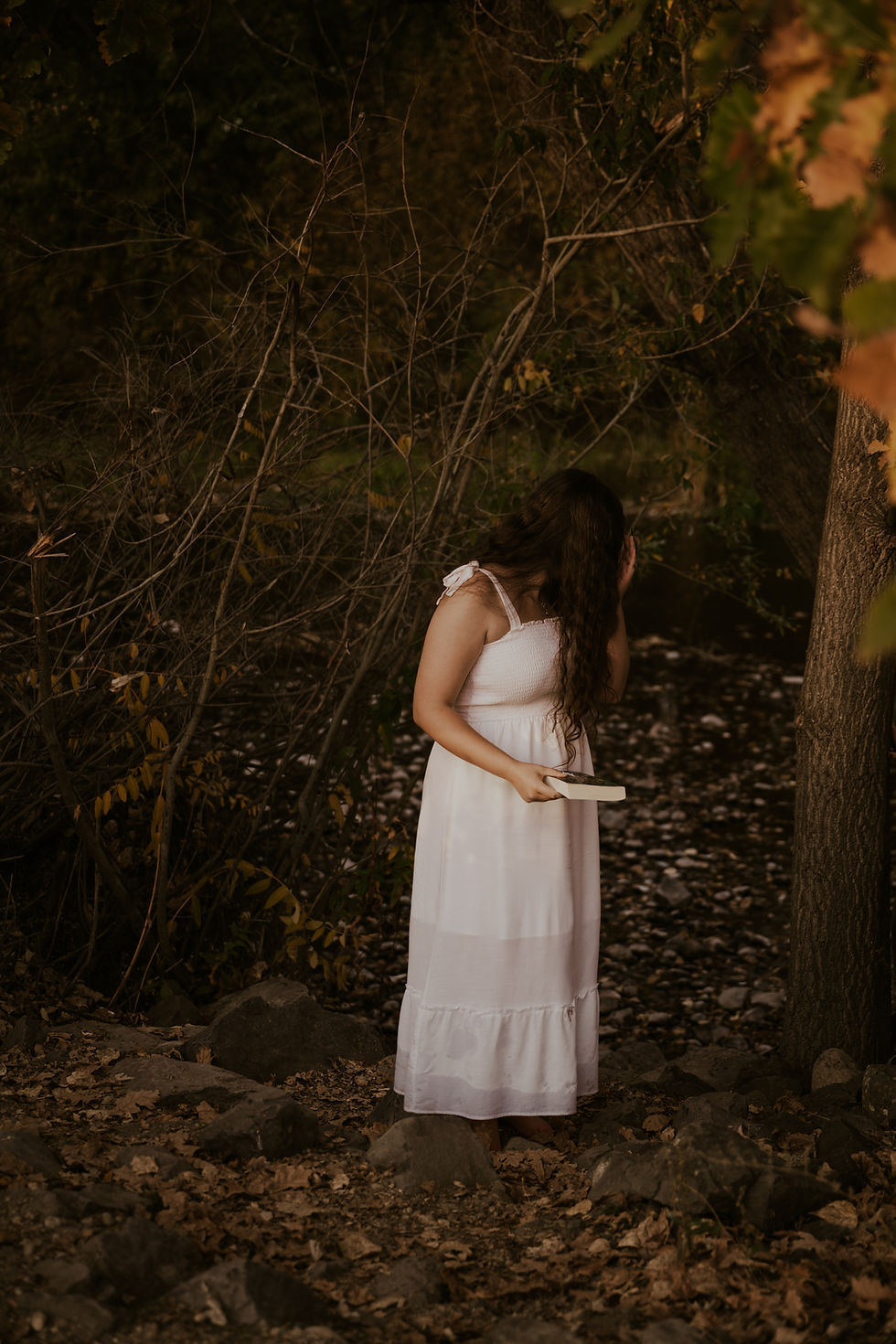 young woman in white dress in river holding a book