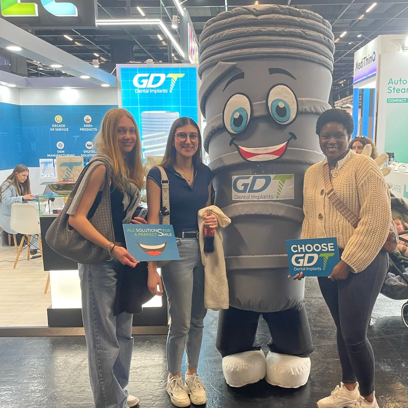 3 dental students posing with smiling infront of the GDT Booth at IDS Cologne 2025