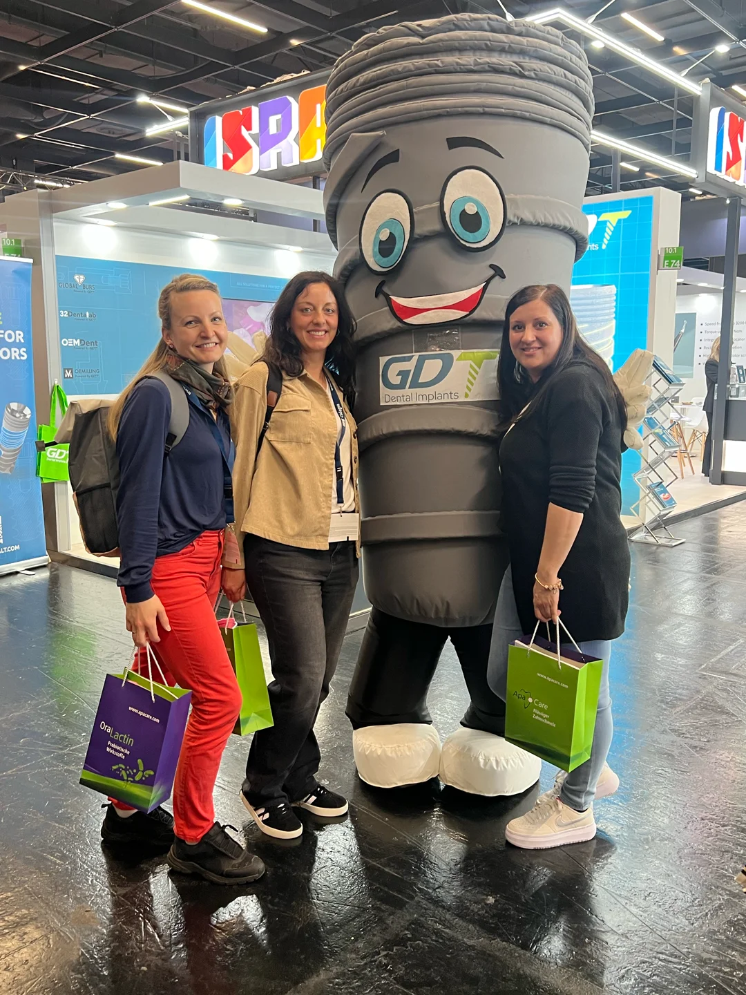 3 women posing and happy to take a photo with smilix - infront of the GDT Booth in IDS Cologne 2025