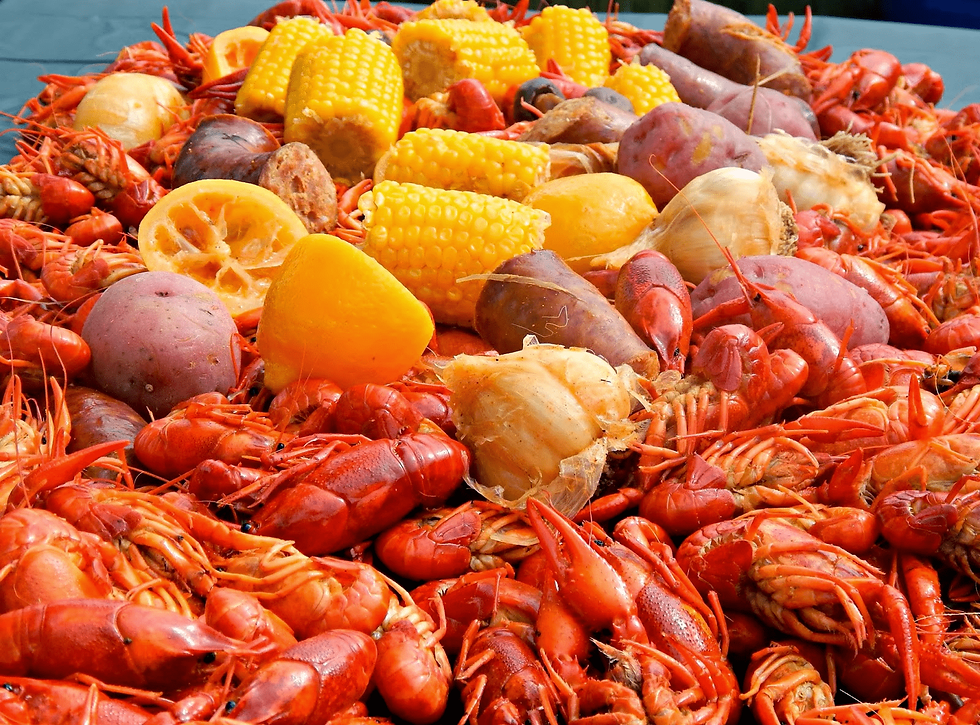 Red crawfish piled with corn, potatoes, and lemon wedges in a seafood boil on a tray outdoors.