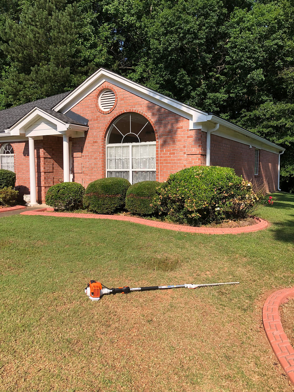 Front yard of a brick house with shrubs and lawn care tool on the grass, landscape orientation