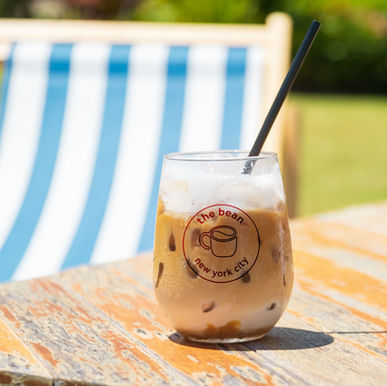 The Bean NYC Redesigned Logo In Maroon On Stemless White Wine Glass Filled With Iced Coffee