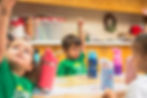 Gan Sinai preschool students raising their hands during a classroom group activity.