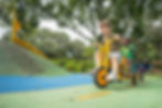 Gan Sinai students riding pedal go-karts together on the playground during outdoor activity.