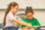 Older student helping a younger student with a hands-on learning activity at Sinai Learning Lab.
