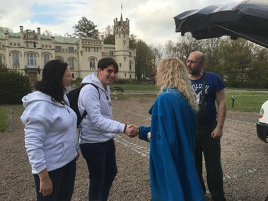 Four people standing and a castle in the background, and two of them shaking hands.