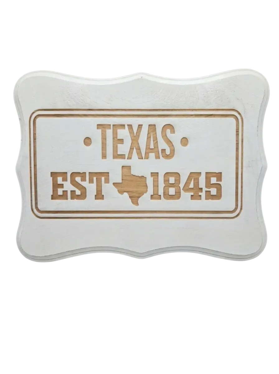 Carved wood sign displaying 'Texas EST 1845' with the outline of the state. Features a rustic, decorative aesthetic.