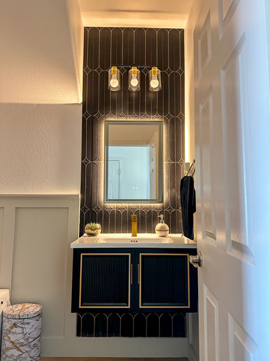 Modern Art Deco bathroom featuring a backlit mirror, geometric accent wall, and black-gold vanity.
