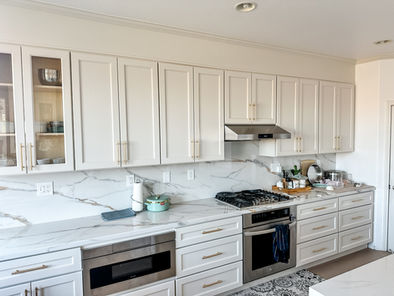 Art Deco kitchen with white cabinetry, elegant marble countertops, and gold hardware.