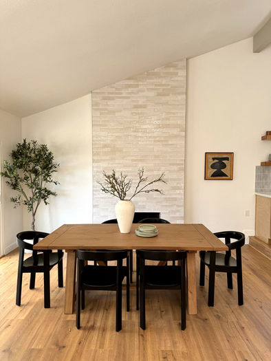 Dining space with wood floors, black chairs, and textured tile chimney reaching up to the ceiling