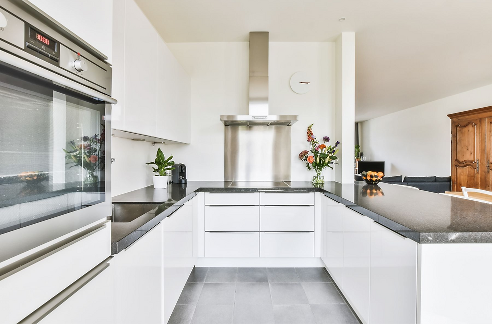 Modern kitchen featuring sleek white cabinets, a built-in oven, a stainless steel range hood, and a large black countertop with decorative flowers on display.