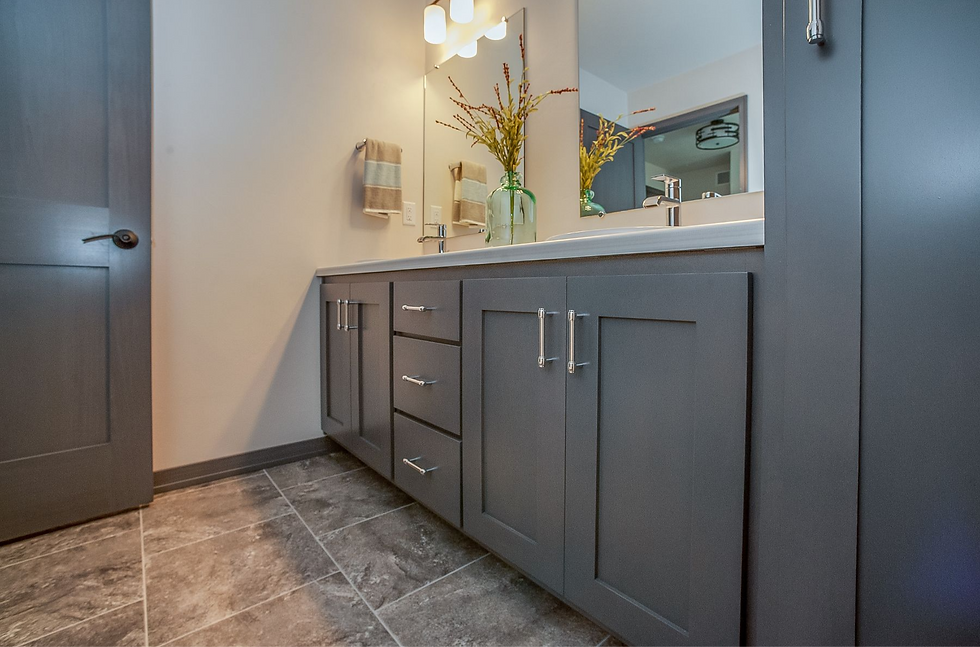 Modern bathroom with dark gray cabinetry, a white countertop, and a stylish vanity sink. The room features sleek hardware, a decorative vase with flowers, and textured flooring for a contemporary look.