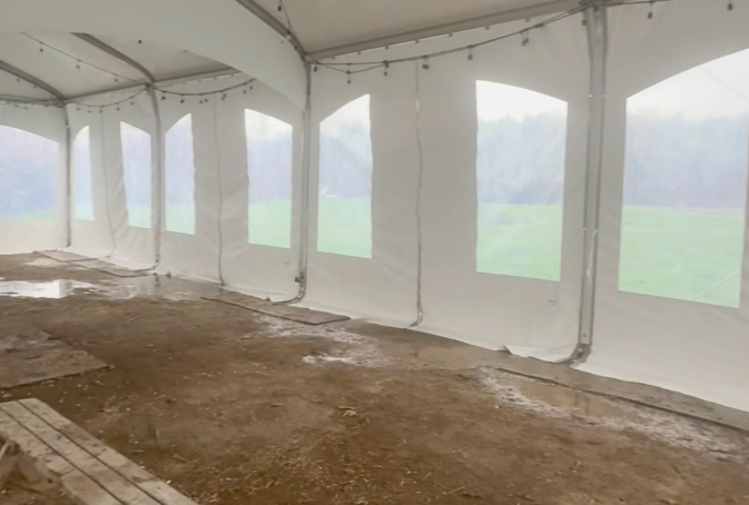 Empty white event tent with muddy floor, windows looking onto a foggy green field, calm and overcast mood