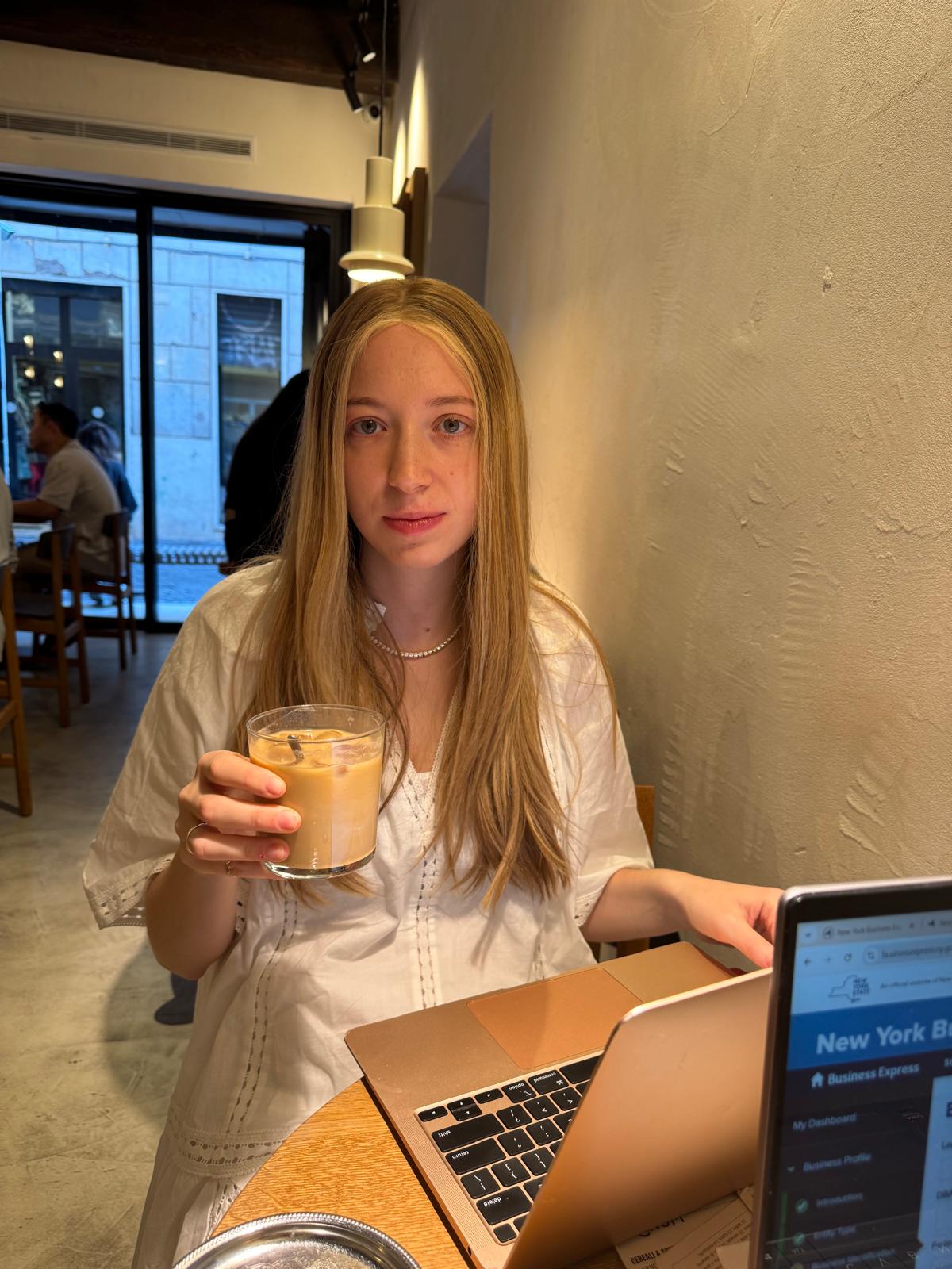 Devora Meroz with an iced coffee at her laptop in a café