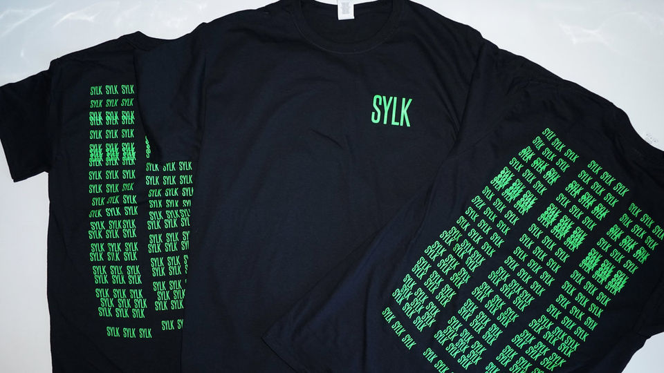 Black t-shirt with neon green 'SYLK' logo in top right corner on the front and multiple overlapping neon green 'SYLK' logos c
