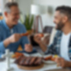 Two Christian men sharing a meal of ribs and wings, smiling and enjoying fellowship together, with a small cross on the table symbolizing their shared faith