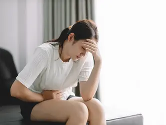 Young asian woman stomach ache sitting on bed at home