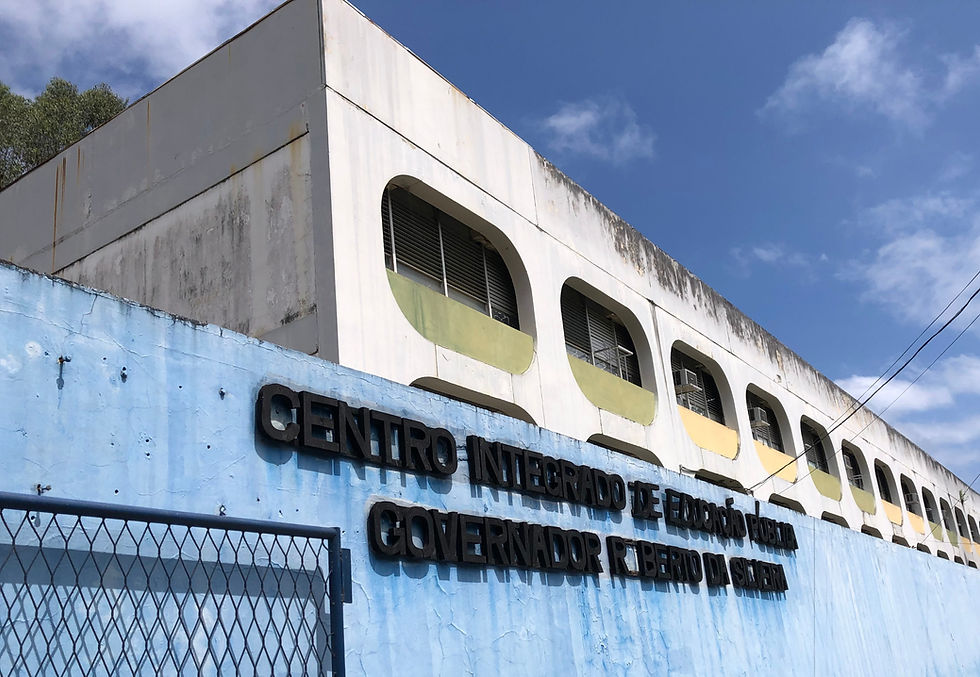 A foto mostra o CIEP Governador Roberto da Silveira, escola de Rio das Pedras, o muro azul com o nome da escola escrito e um portão de grades que dá acesso à ele.