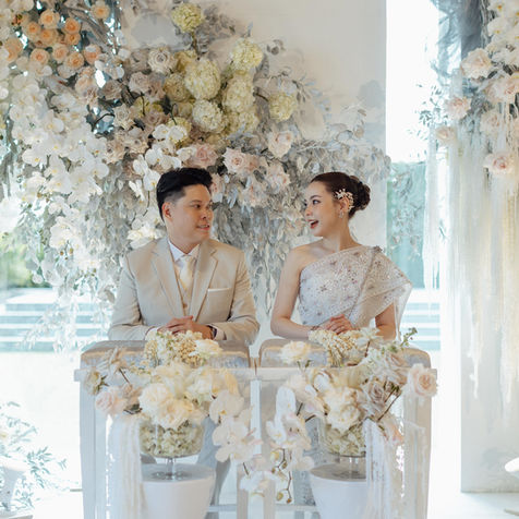 The couple looking at each other and smiling happily while participating in their traditional Thai wedding ritual.