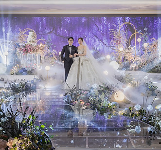 Grand wedding stage with purple and white flowers, shimmering lights, and elegant hotel ballroom decor.