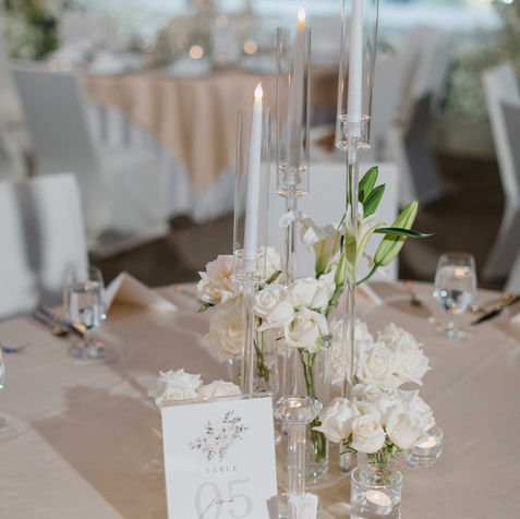 A detailed shot of an elegant reception table centerpiece featuring white flowers and tall glass candles.