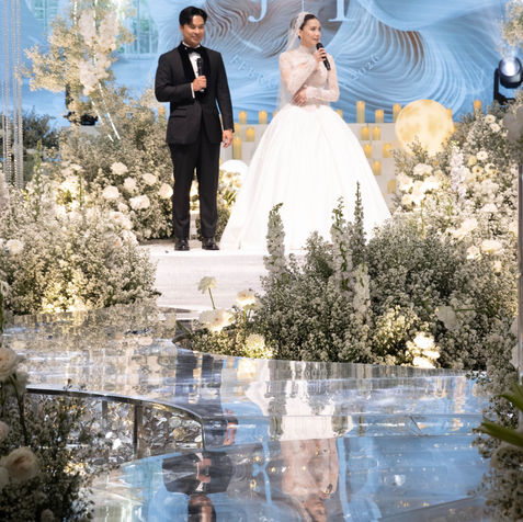 Beautiful wide shot of the newlyweds standing in the center of the stage, perfectly reflected in the glossy floor surface.