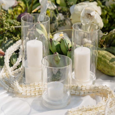 Table centerpiece detail showing thick white pillar candles in glass holders surrounded by strings of decorative pearls.