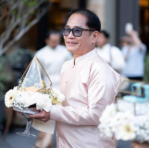 A smiling wedding guest holding a decorative traditional Thai Khan Mak ceremonial tray.