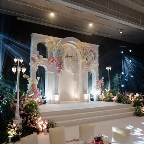 A long navy-blue wedding runway corridor lined with lush flower bushes and glowing glass globes under dimmed lights.